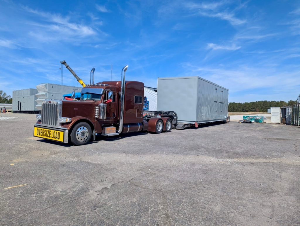 Heavy haul tractor-trailer transporting a prefabricated equipment enclosure module.