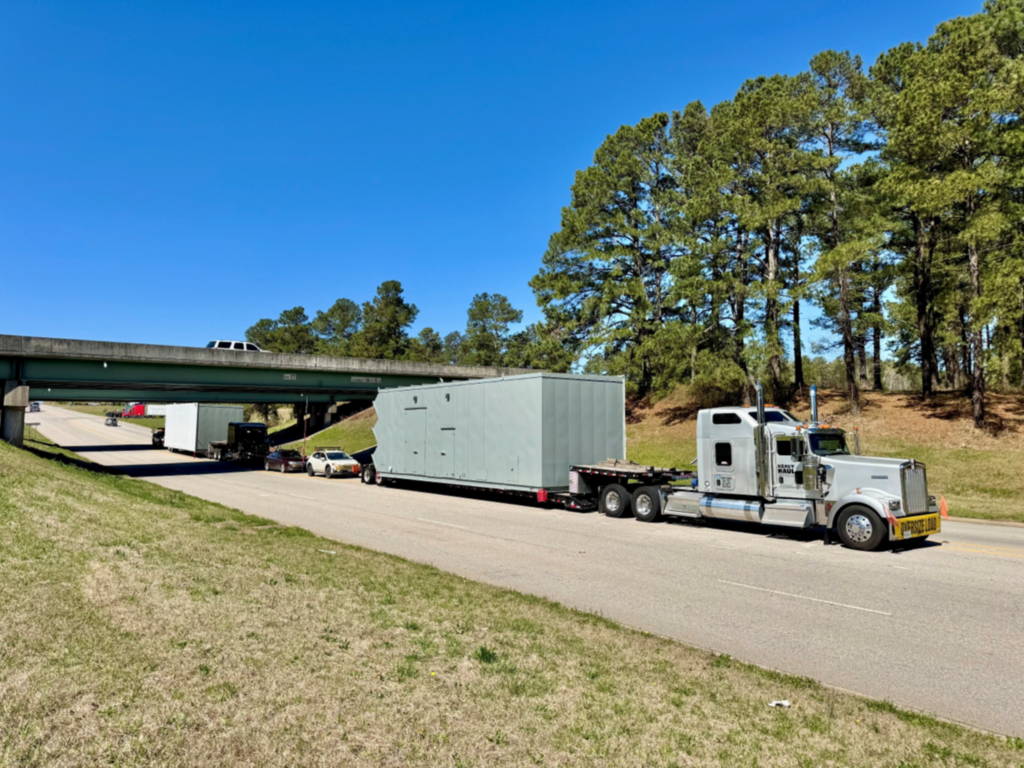 Heavy haul truck transporting a large modular building on a trailer with escort vehicles.