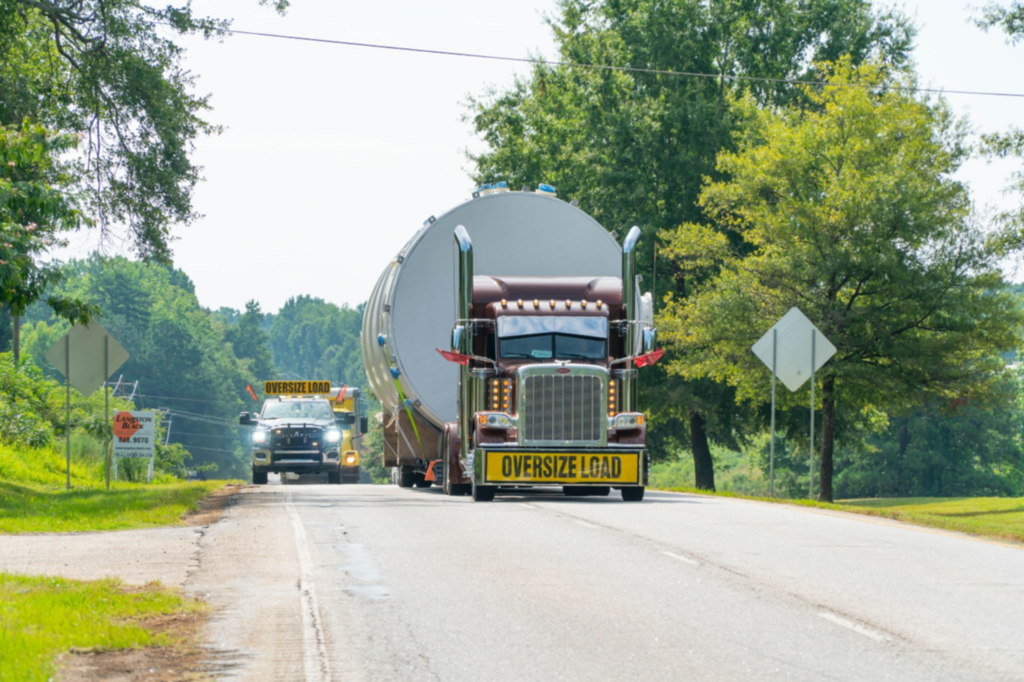 Oversize load truck hauling a large industrial tank with escort vehicle for heavy transport.