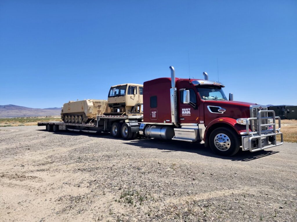 Heavy haul semi truck transporting military armored vehicle on lowboy trailer. Asset-based 3PL specialized freight